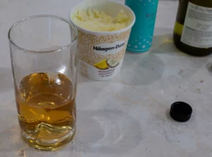 White wine in a tall glass and ice cream on the back.
